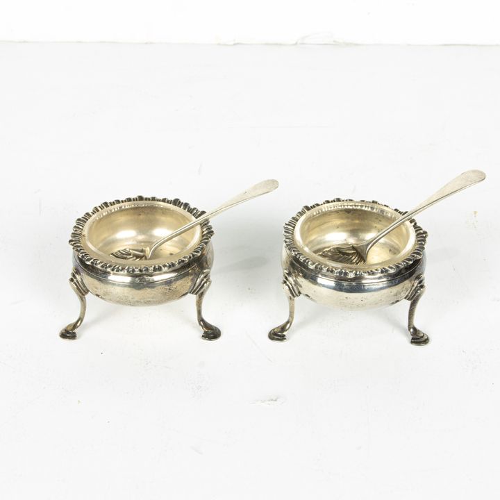 A pair of Georgian sterling open salts having a gadrooned rim and rising on padded feet en suite with shell bowl salt spoons by Thom...