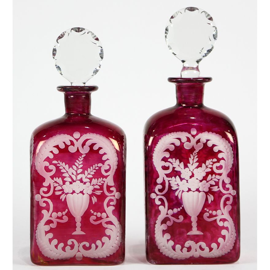 Pair of Bohemian blown glass decanters, executed in ruby, each having a faceted circular stopper above the body, having frosted deco...